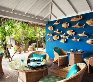 Open-air tropical restaurant with wicker seating, blue accent wall, and handcrafted wooden fish décor.