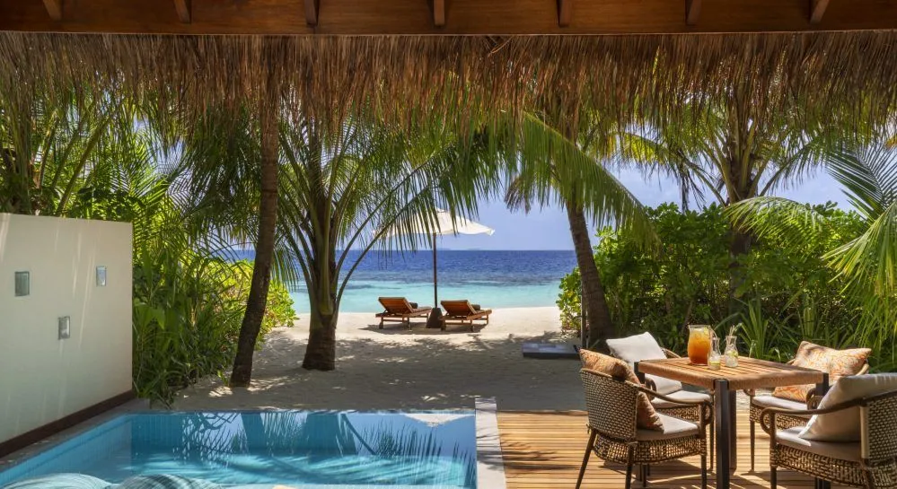 Luxury beachfront villa in the Maldives featuring a private plunge pool, outdoor dining area, swaying palm trees, and direct access to a white sandy beach with turquoise ocean views.