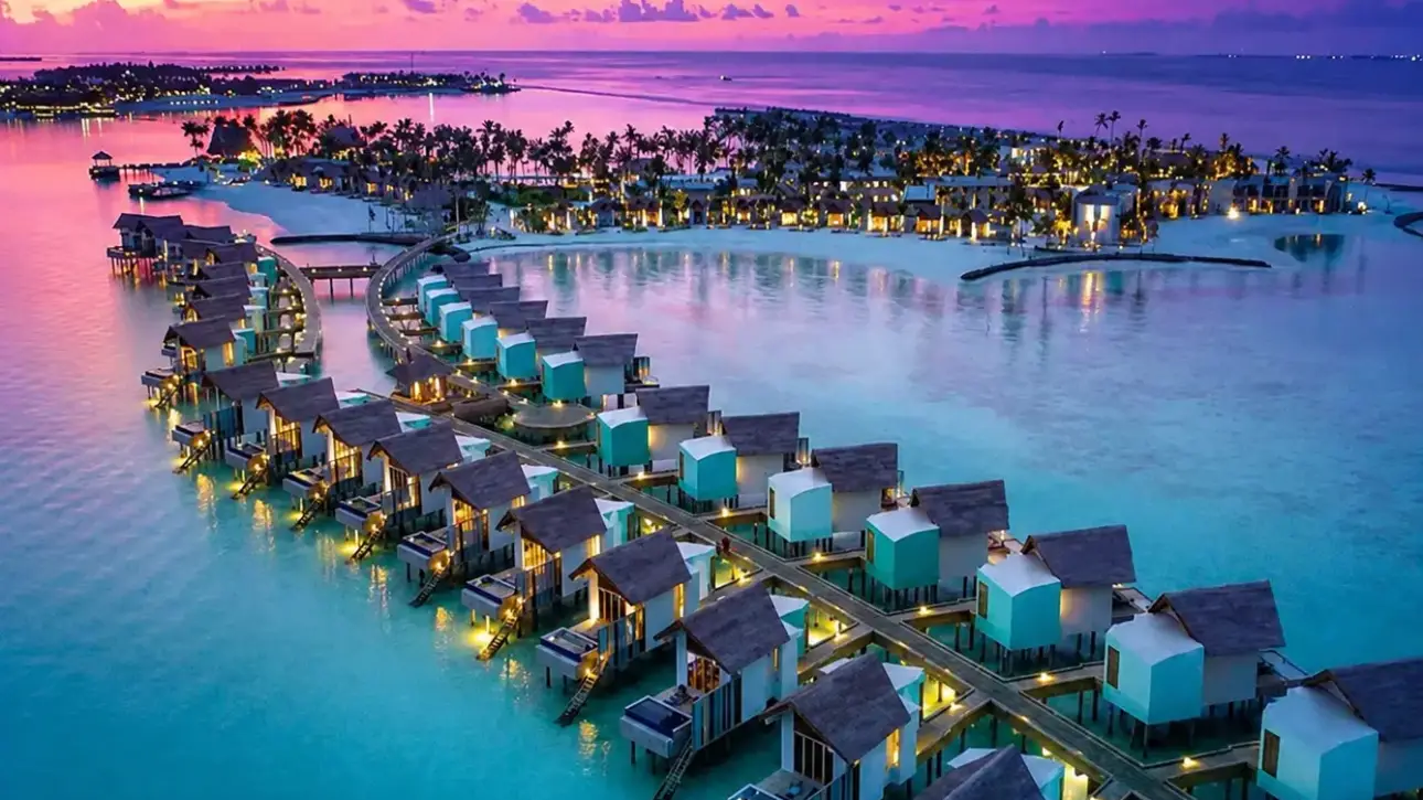 Luxury overwater villas at a Maldives resort overlooking a turquoise lagoon during a vibrant sunset.
