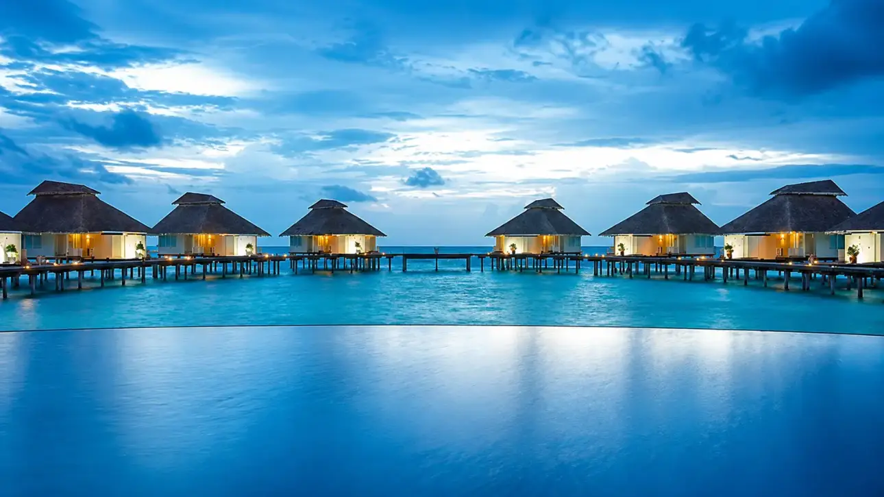 Luxury Maldives resort with an infinity pool, overwater villas, and a stunning ocean view at dusk.