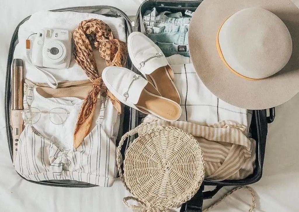 Open suitcase packed with Maldives vacation essentials, including beachwear, camera, hat, shoes, and travel accessories.