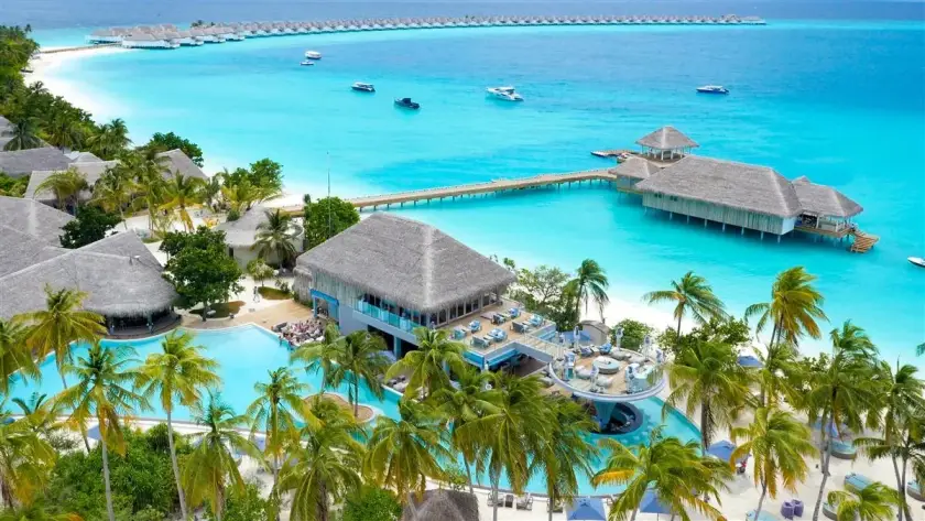 Traditional boat sailing through turquoise water near a tropical Maldives island with a white sand beach.