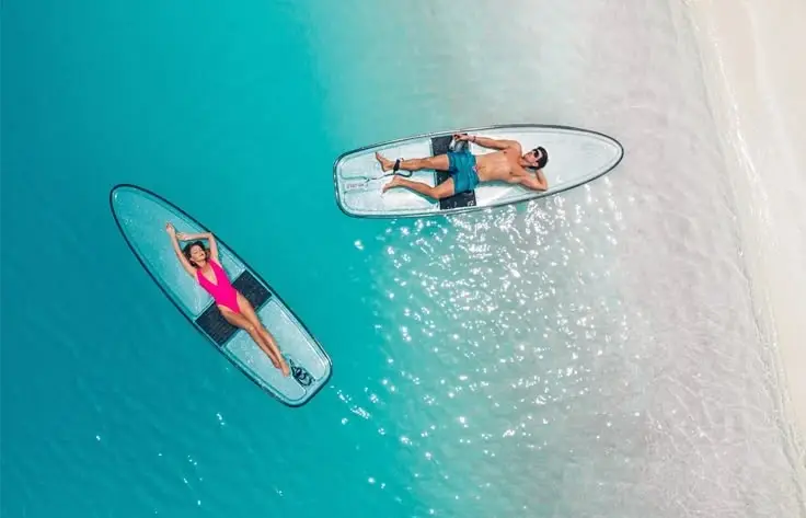 Two people relaxing on paddleboards in clear turquoise waters near a tropical beach