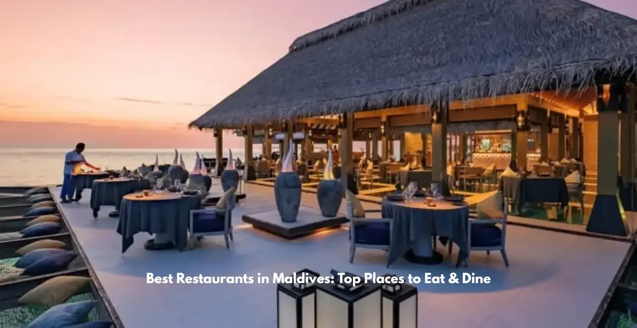 Open-air thatched-roof restaurant beside the ocean in the Maldives, with elegantly set tables overlooking a sunset.