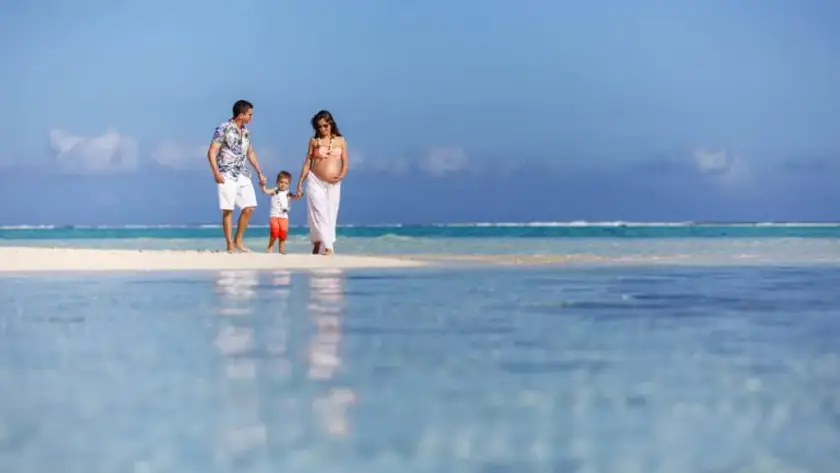 Pregnant couple with their young child walking along a tropical Maldives beach