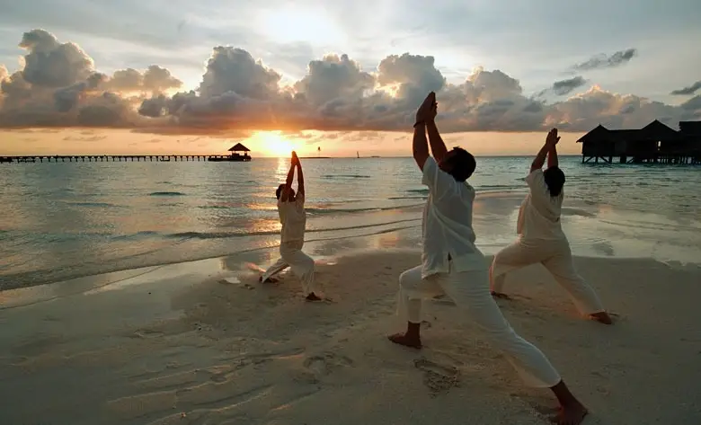 Beach yoga session at a Maldives wellness resort overlooking the ocean at sunset