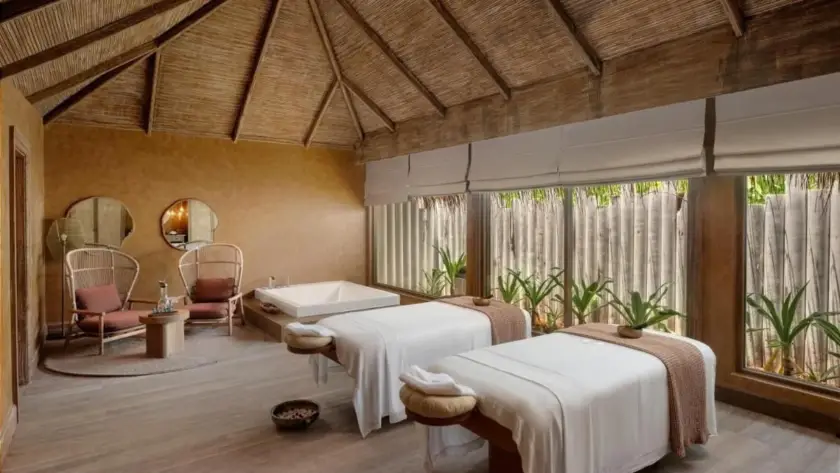 Luxury wellness spa in the Maldives featuring twin massage beds, a traditional thatched ceiling, and a peaceful tropical setting