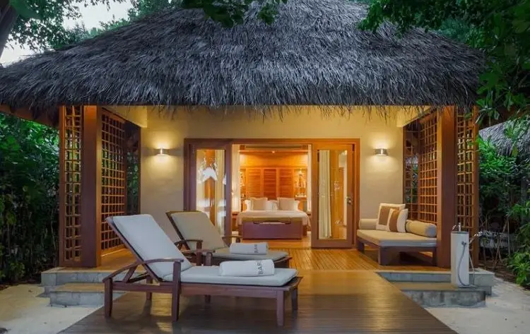 Luxury Maldives wellness resort villa with a thatched roof, private wooden deck, and sun loungers surrounded by tropical greenery